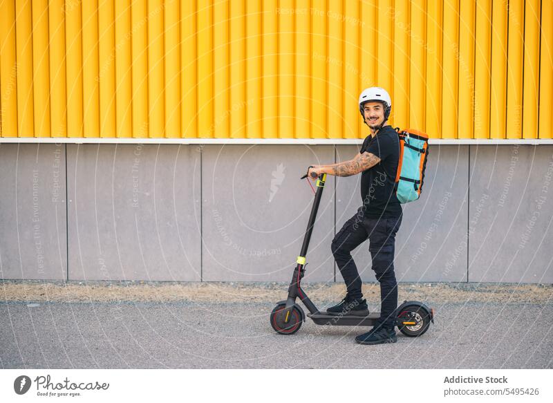 Kurierdienstmitarbeiter mit Elektroroller auf der Straße schaut in die Kamera Auslieferer Kickroller elektrisch Mitfahrgelegenheit Verkehr Dienst Arbeiter