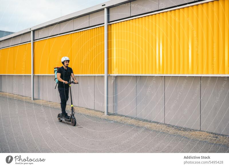 Kurierdienstmitarbeiter fährt mit Elektroroller auf der Straße Auslieferer Kickroller elektrisch Mitfahrgelegenheit Verkehr Dienst Arbeiter Tretroller Großstadt