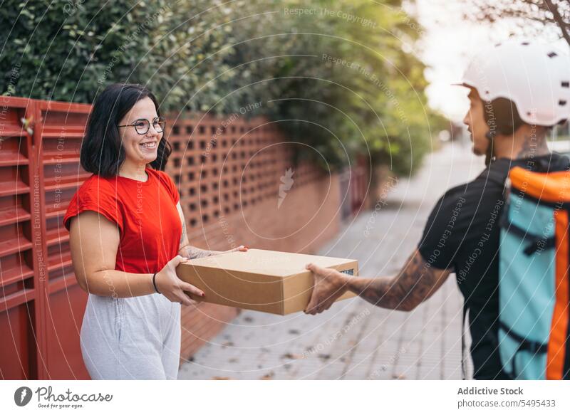 Zufriedener Kunde, der ein Paket vom Kurier auf dem Bürgersteig erhält Frau Auslieferer Empfang Karton Kasten Kollo Lächeln Dienst Versand behüten Mann