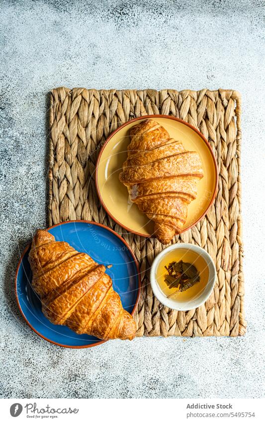 Frisch gebackene Croissants auf Keramiktellern frisch Teller farbenfroh braun Serviette Tasse grün Tee Tisch Oberfläche grauer Hintergrund hoher Winkel von oben