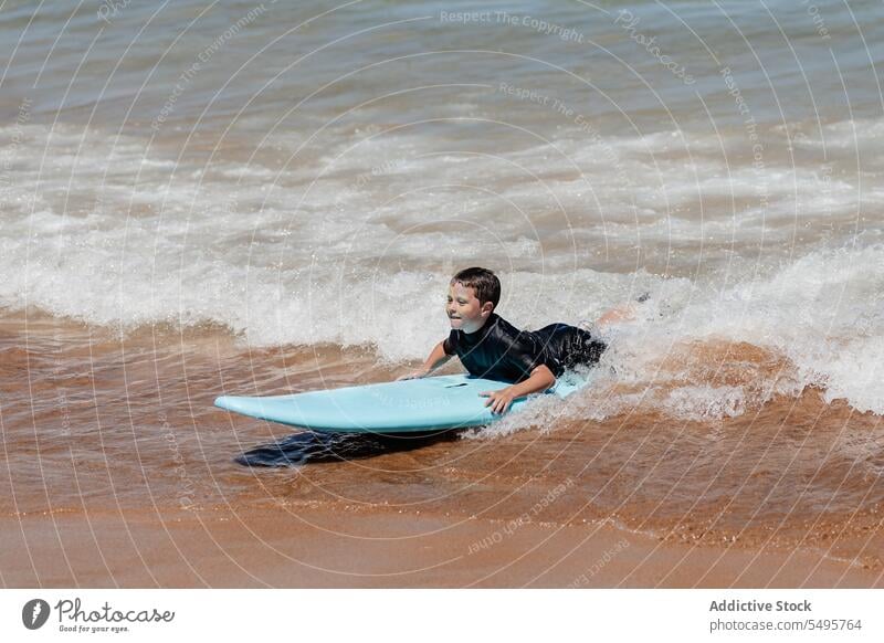 Kind mit Surfbrett im Meer Junge Surfer schwimmen MEER winken Lügen Surfen Sommer männlich Urlaub Meereslandschaft Natur Glück Zusammensein spielerisch Wasser