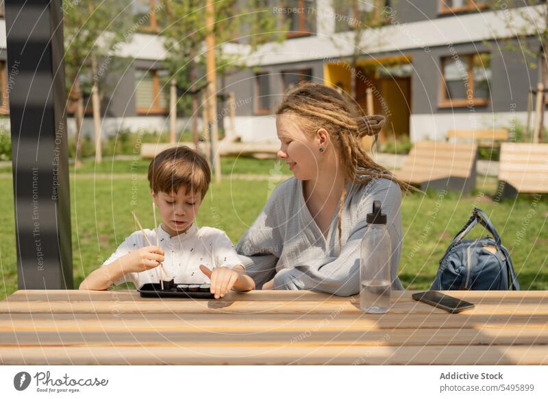 Frau sitzt mit Junge und isst Sushi im Park im Sommer Mutter Sohn essen Lächeln Tisch Familie Lebensmittel Liebe Lifestyle Rastalocken Sitzen niedlich