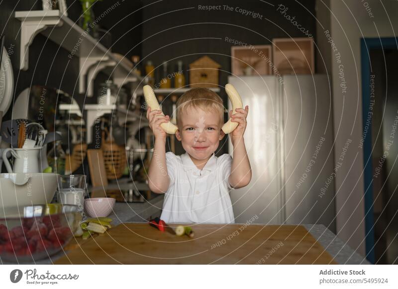 Süßer Junge hält Bananen und lächelt in der Küche Lächeln Essen zubereiten niedlich Porträt Kind Frucht Vorbereitung Lifestyle Lebensmittel Unschuld Kindheit