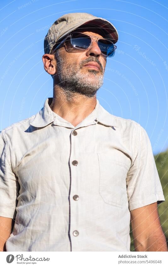 Selbstbewusster bärtiger Mann mit Sonnenbrille und Mütze selbstbewusst Sommer Blauer Himmel Verschlussdeckel ernst Vollbart brutal Vorschein männlich unrasiert