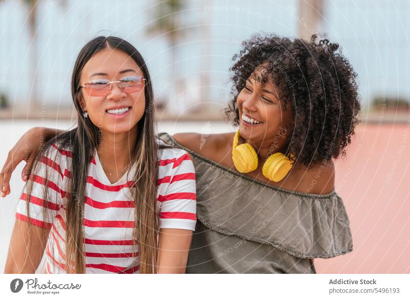 Glückliche junge Frauen, die sich auf der Straße in der Stadt umarmen und lächeln Freundin Stil Umarmen Lachen Partnerschaft Zusammensein heiter cool Lächeln