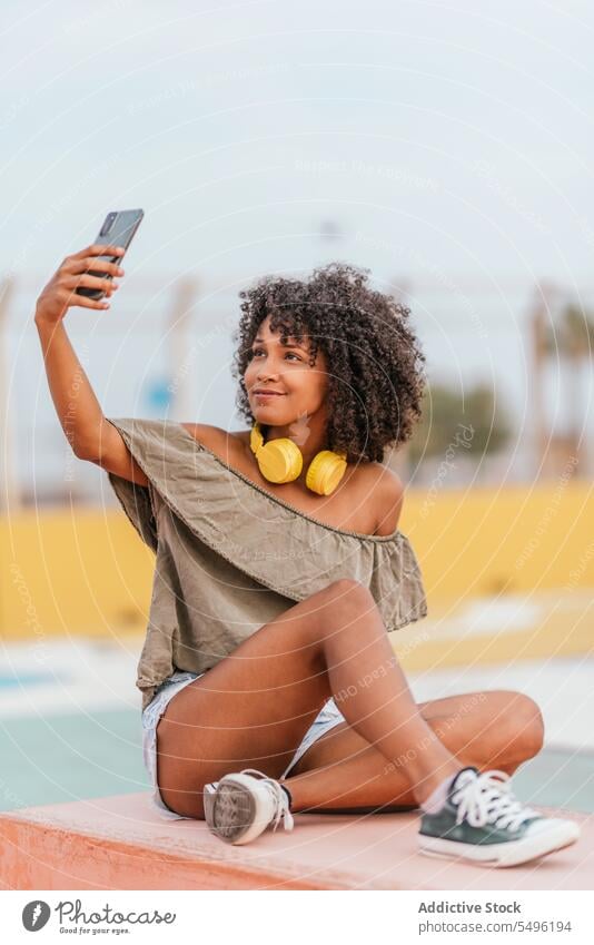 Lächelnde junge Frau mit Kopfhörern, die ein Selfie mit ihrem Smartphone macht Telefon benutzend zuhören Mobile Glück positiv Bank Gerät Straße genießen