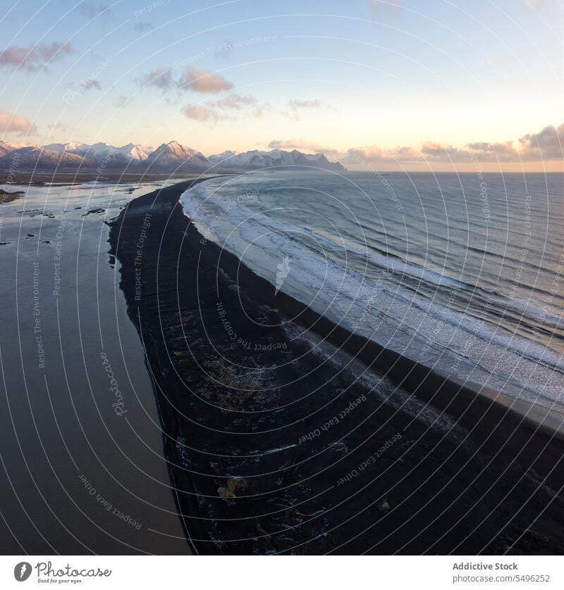 Erstaunlicher Blick auf die felsige Küste mit welligem Meer und schneebedeckten Bergen bei Sonnenuntergang Berge u. Gebirge Meereslandschaft Landschaft MEER