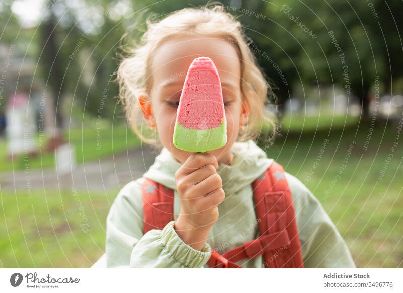 Mädchen mit Rucksack steht in der Nähe grasbewachsenen Feld und genießt Eis Kind Speiseeis Park Weg niedlich Kindheit grün bezaubernd Sommer süß sorgenfrei