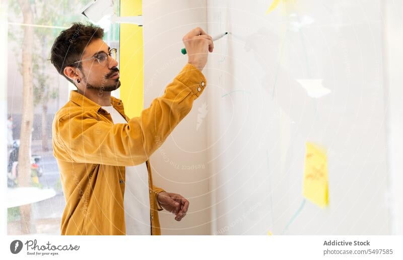 Fokussierter ethnischer Mann schreibt auf Whiteboard schreiben Büro Markierung ernst professionell Plan zur Kenntnis nehmen Business männlich Arbeit Job Projekt