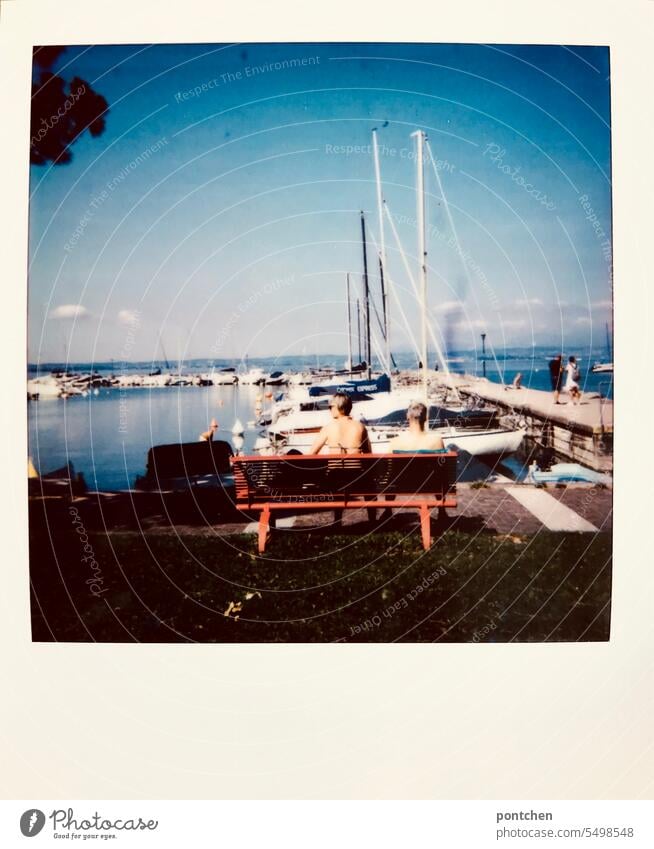 ein paar in badebekleidung sitzt am hafen auf einer roten bank. gardasee polaroid ausblick senioren rücken boote Außenaufnahme Tourismus