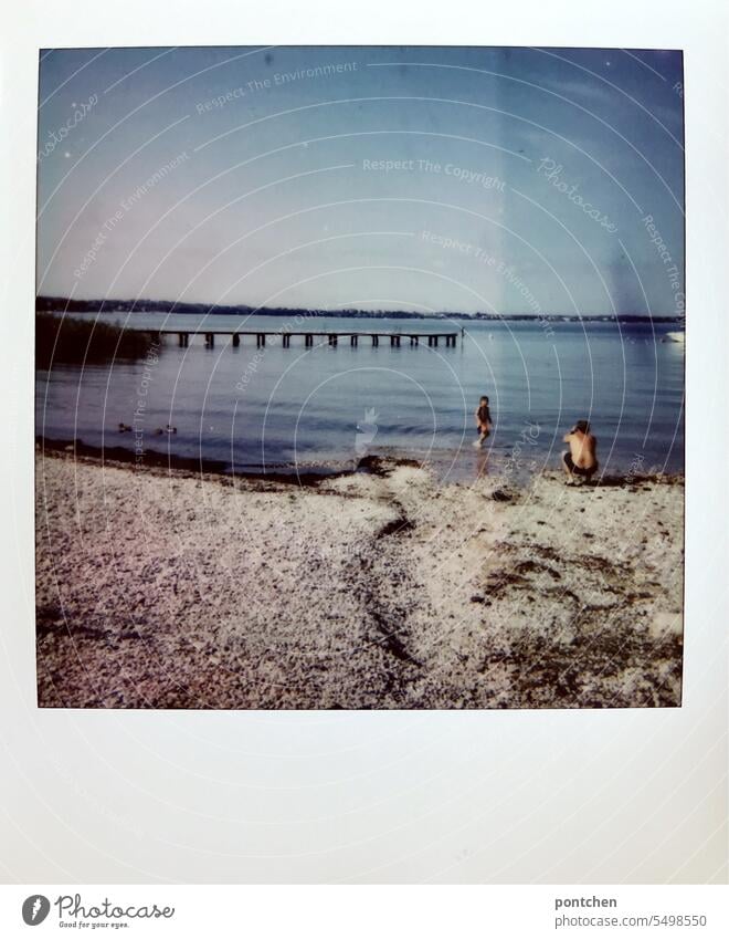 ein vater am seeufer in der hocke fotografiert seinen sohn, der im wasser steht. polaroid Seeufer Schönes Wetter Sommer Gardasee himmel Ferien & Urlaub & Reisen