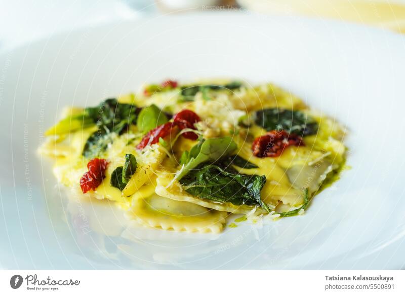 Italienische Ravioli mit Basilikum, Spinat, sonnengetrockneten Tomaten, Pinienkernen und Käse in einem weißen Teller. Traditionelle italienische Küche im Restaurant