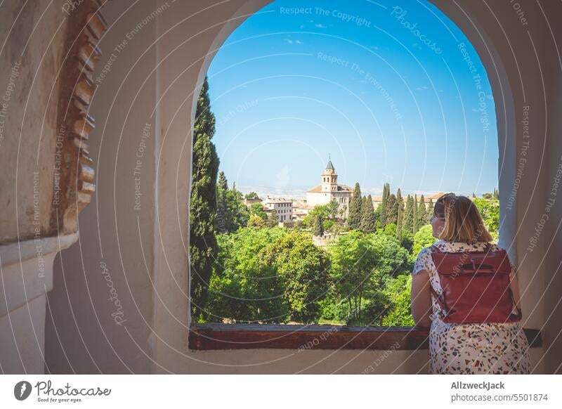 kaukasische Frau mittleren Alters mit blonden Haaren und Rucksack auf dem Rücken schaut in Andalusien aus dem Fenster auf eine malerische Szenerie Spanien