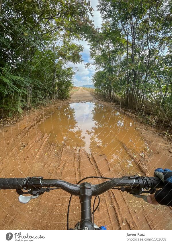 Blick aus der ersten Person auf den Lenker eines Mountainbikes kurz vor dem Überqueren einer großen Pfütze aus Schlamm und Wasser auf einem Waldweg Teich Fleck