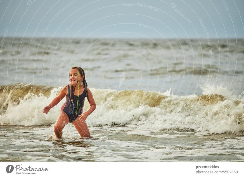 Kleines Mädchen spielt mit Wellen im Meer. Kind plantscht spielerisch in Wellen. Kind springt ins Meer. Urlaub am Strand. Wasser plätschert Sommer Ferien MEER