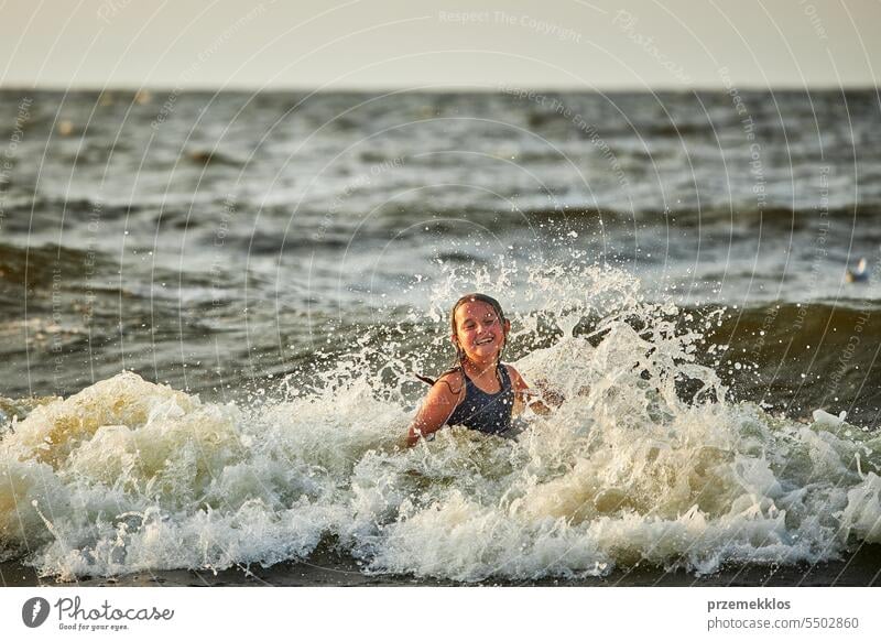 Kleines Mädchen spielt mit Wellen im Meer. Kind plantscht spielerisch mit Wellen. Kind springt in Meereswellen. Sommerurlaub am Strand Ferien MEER Spielen