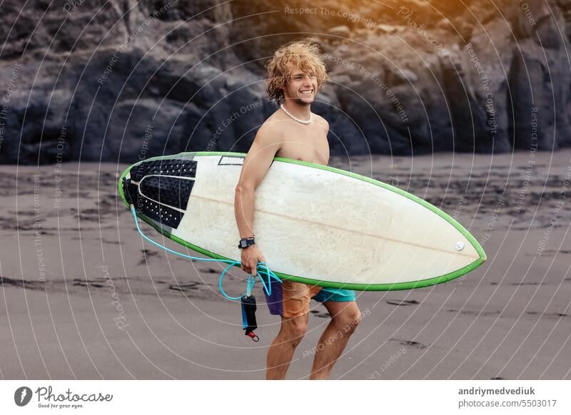 Fit jungen Surfer Mann mit lockigem blondem Haar mit Surfbrett geht durch den Ozean Spaß haben extreme Wassersportarten, Surfen. Reisen und gesunden Lebensstil Konzept. Sport Reiseziel.