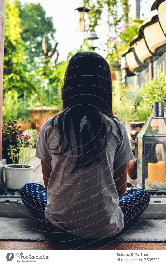 Kind mit langen Haaren sitzt an der offenen Balkontür und schaut auf den begrünten Balkon Terrasse Langeweile zuhause zu Hause Familie Sitzen Schneidersitz