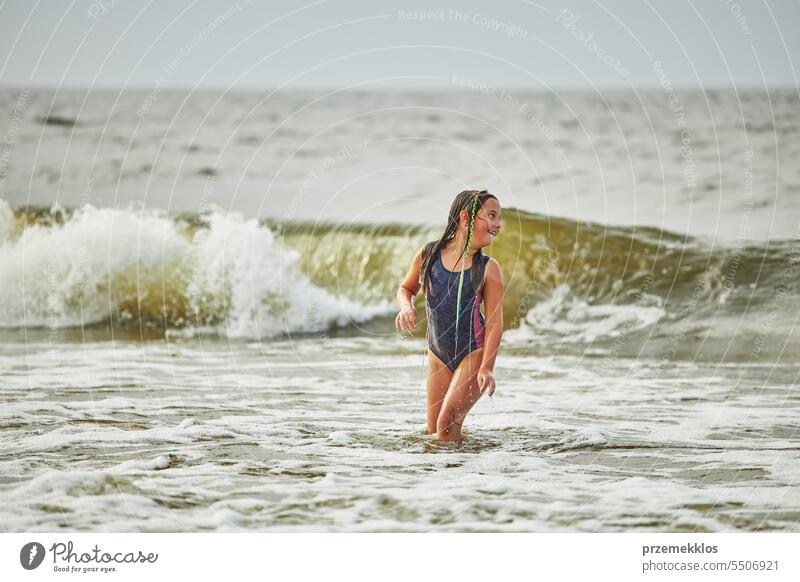 Kleines Mädchen spielt mit Wellen im Meer. Kind plantscht spielerisch in Wellen. Kind springt ins Meer. Urlaub am Strand. Wasser plätschert Sommer Ferien MEER