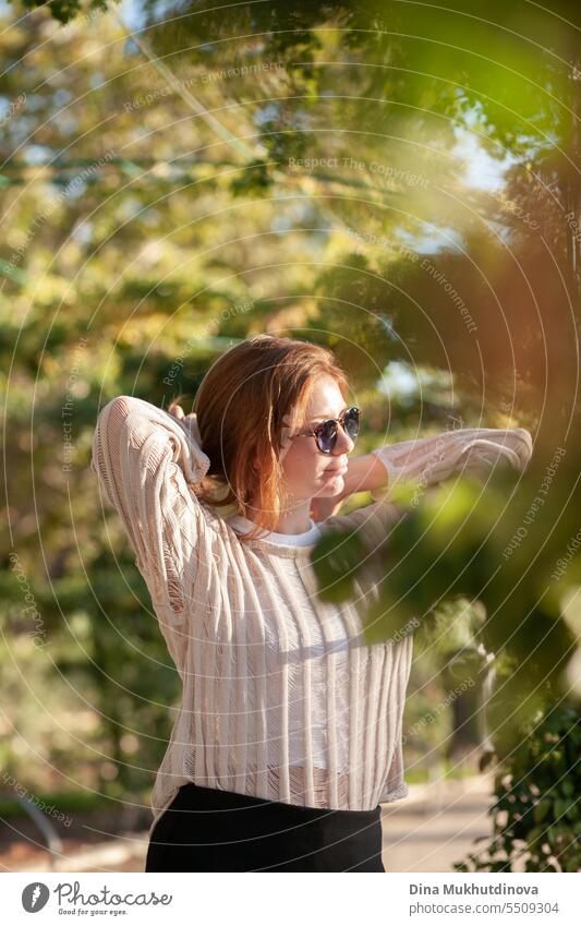 candid Porträt der jungen schönen Frau mit Sonnenbrille im Gegenlicht mit Sonnenlicht im Sommer. Hübsches rothaariges Mädchen mit roten Haaren. Park Lächeln