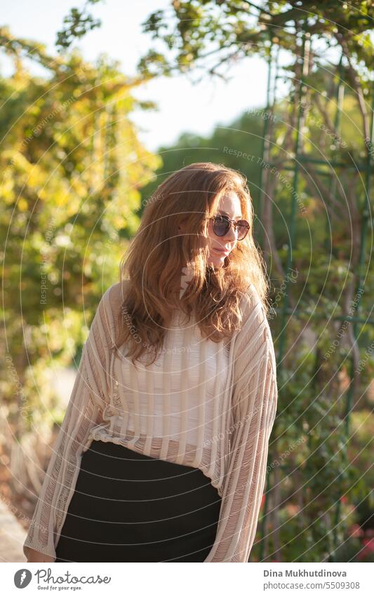 candid Porträt der jungen schönen Frau mit Sonnenbrille im Gegenlicht mit Sonnenlicht im Sommer. Hübsches rothaariges Mädchen mit roten Haaren. Park Lächeln