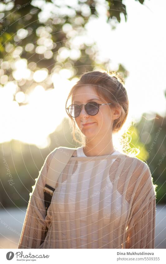 candid Porträt der jungen schönen Frau mit Sonnenbrille im Gegenlicht mit Sonnenlicht im Sommer. Hübsches rothaariges Mädchen mit roten Haaren. Park Lächeln