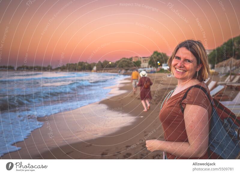 Portrait einer lächelnden blonden Frau mittleren Alters am Strand zum Sonnennuntergang Sonnenuntergang Sonnenuntergangshimmel Abendrot blondes Haar Lächeln