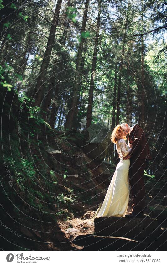 Glückliche stilvolle Paar Jungvermählten in den grünen Wald am Sommertag. Braut in langen weißen Kleid und Bräutigam im roten Anzug sind umarmt. Park Tag