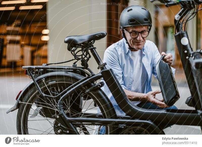 Älterer Mann wechselt die Batterie an seinem Elektrofahrrad Menschen Kaukasier Gesundheit Stadtleben graues Haar genießen Straße lässig Tag Porträt außerhalb