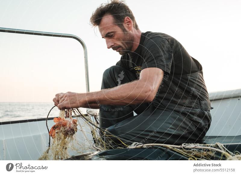 Anonymer Mann, der mit der Hand die Fäden des Fischernetzes entwirrt, um bei Tageslicht Fische zu fangen Netz Fischen Boot Wasser Schiffsdeck Gerät Natur