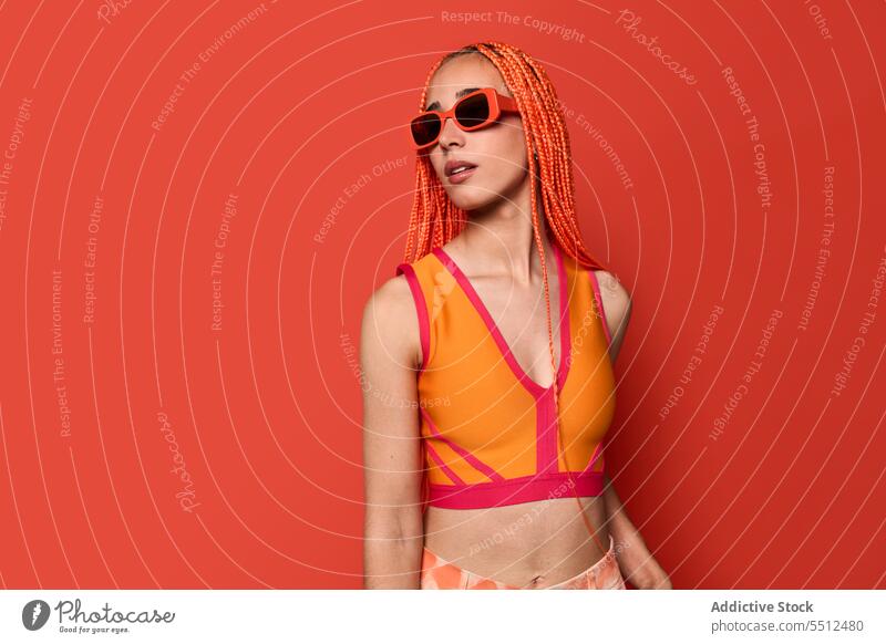 Stylische Frau in orangefarbenem Outfit und Sonnenbrille selbstbewusst stylisch Mode Model Studioaufnahme emotionslos cool lebhaft Vorschein jung Afro-Zöpfe Top