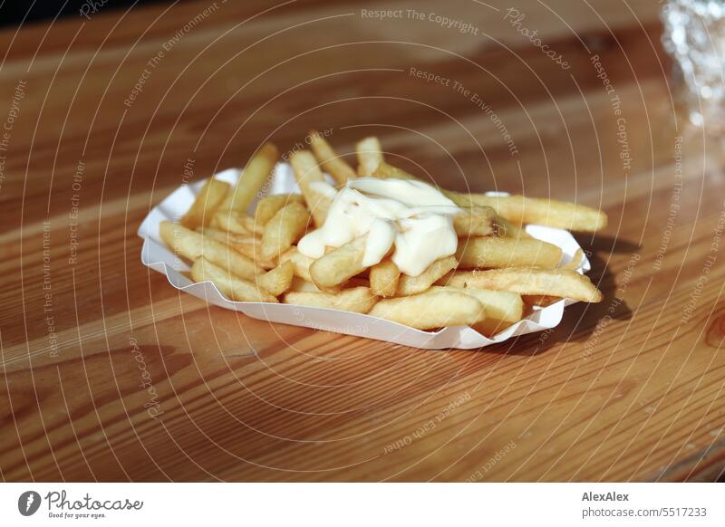 Pommes Frites mit Mayonnaise in einer weißen Pommesschale auf einem Biertisch aus Holz Kartoffeln Fast Food Fastfood Essen fettig reichhaltig kcal Kalorien