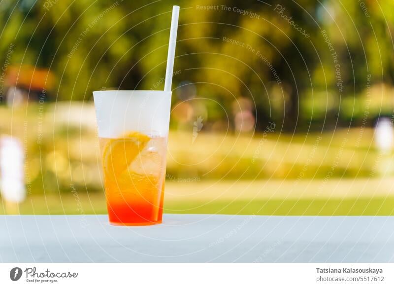 Ein Glas mit einem erfrischenden Sommercocktail auf einem verschwommenen natürlichen grünen Hintergrund trinken Cocktail orange Getränk gelb