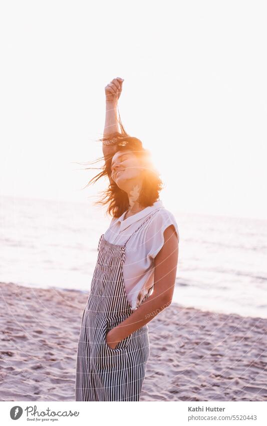 Eine junge Frau am Meer mit Wind in den Haaren und dem Sonnenuntergang. Strand Abend Wasser Mensch Himmel Silhouette Schatten Dämmerung Farbfoto Küste