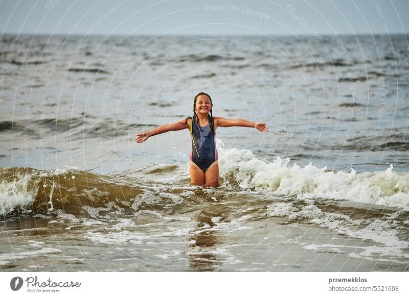 Kleines Mädchen spielt mit Wellen im Meer. Kind plantscht spielerisch in Wellen. Kind springt ins Meer. Urlaub am Strand. Wasser plätschert Sommer Ferien MEER