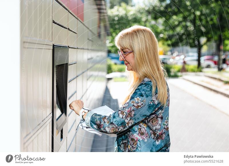 Reife Frau benutzt Paketkasten in der Stadt natürlich genießen zufrieden heiter selbstbewusst Freude Rentnerin im Freien außerhalb Brille älter Fröhlichkeit