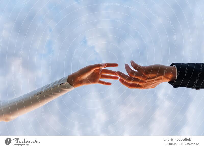 Hände der Braut im weißen Kleid und Bräutigam im Anzug erreichen einander, berühren Finger auf blauem Himmel Hintergrund. Helfende Hände für speichern und unterstützen Menschen Konzept. Hochzeitstag. Valentinstag.