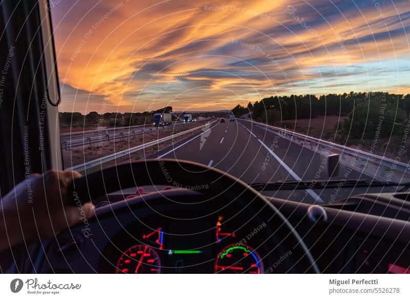 Blick aus dem Fahrersitz eines Lkw auf eine Autobahn mit Fahrzeugen in beiden Richtungen unter einem dramatischen Himmel. Lastwagen Hand im Inneren Kabine