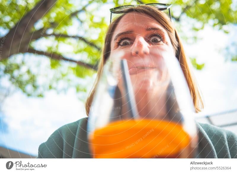 junge blonde Frau macht Grimassen durch ein Glas mit Aperol Spritz Junge Frau junge erwachsene blondes Haar Alkohol Alkoholisiert Sommer Sommergetränk