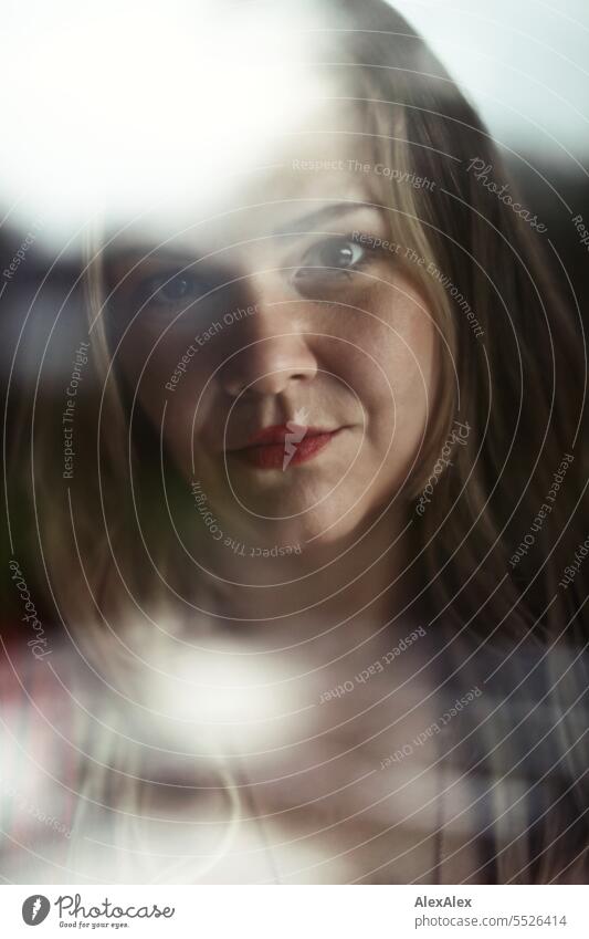 Blonde Frau schaut durch eine Fensterscheibe mit Reflexionen direkt in die Kamera Portrait langhaarig lange Haare Reflexion & Spiegelung Gesicht natürlich schön