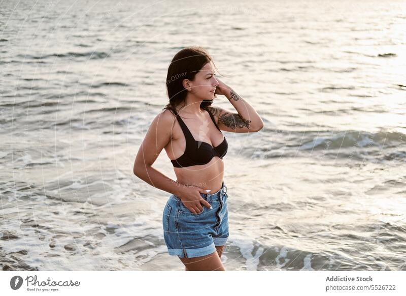 Sorglose Frau in BH und kurzen Jeans am Strand Jeansstoff Shorts Jeanshose MEER Urlaub Stil attraktiv Sommer Meer jung schlank Küste charmant Natur dunkles Haar