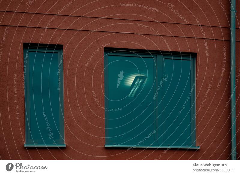 Behind tinted window panes. Blaugrau scheint eine Deckenleuchte durch die getönten Fenster eines Bürogebäudes. Die rotbraune Fassade bildet einen farbigen Kontrast