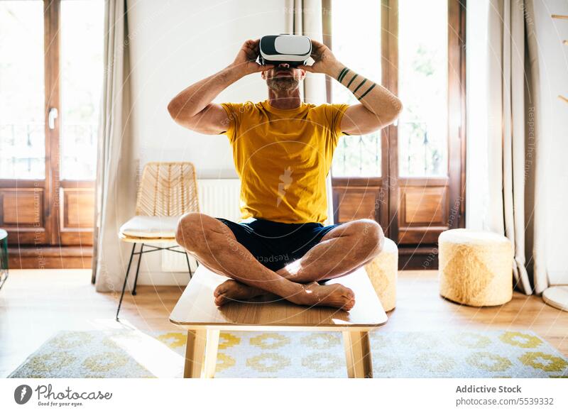 Mann mit VR-Headset trainiert in hellem Raum Yoga Lotus-Pose Virtuelle Realität üben meditieren Schutzbrille männlich digitale Entgiftung Cyberspace Achtsamkeit