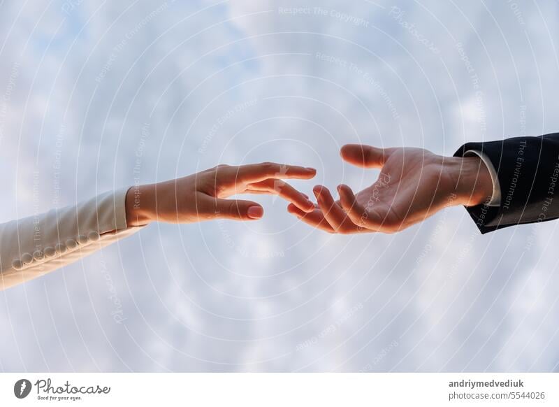 Hände der Braut im weißen Kleid und Bräutigam im Anzug erreichen einander, berühren Finger auf blauem Himmel Hintergrund. Helfende Hände für speichern und unterstützen Menschen Konzept. Hochzeitstag. Valentinstag.