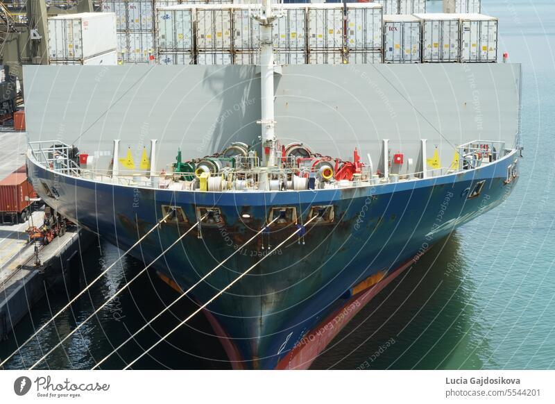 Bug und vorderer Liegeplatz des blauen, voll beladenen Schiffes mit Kühlcontainern längsseits im Hafen von Kingstone unter den Portalkränen während des Ladebetriebs.