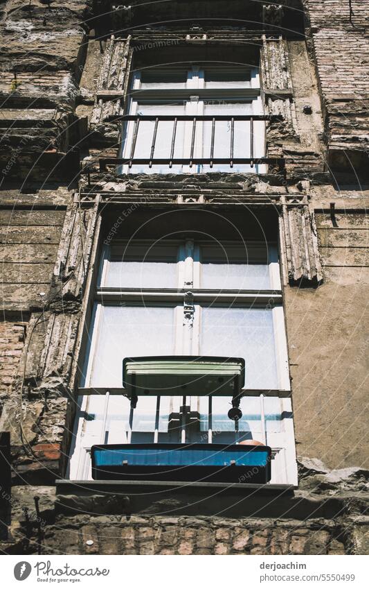 Zwei geschlossene Fenster in einem herunter gekommenden Altbau. Eins mit einem Gitter, das andere Fenster mit zwei leeren Blumenkästen. Fensterrahmen Haus alt