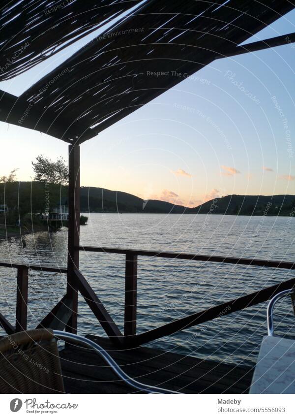 Pavillon mit Bastmatten, Tisch und Stuhl auf einem Bootssteg am Ufer des Poyrazlar See im Sommer im Licht der untergehenden Sonne am bei Adapazari in der Provinz Sakarya in der Türkei