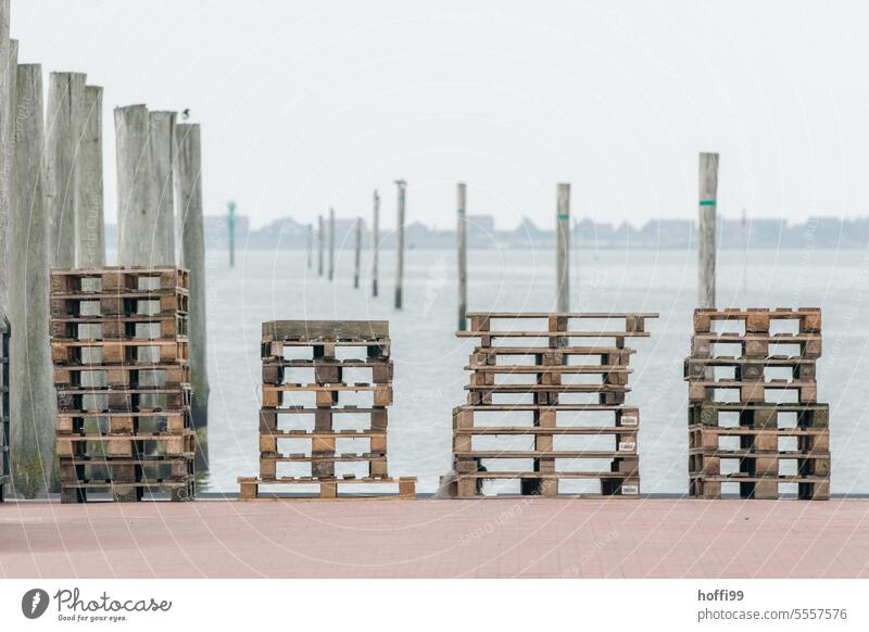 mehrere Stapel von Paletten am Pier im Hafen mit Blick auf eine Insel Europalette Palettenstapel Kaje Fähre Anlegestelle Beladung Nordseeküste Nordseeinsel