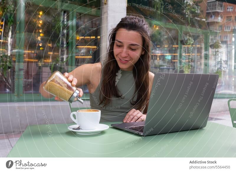 Frau gibt Zucker in eine Tasse Kaffee im Café freiberuflich abgelegen Internet Inbetriebnahme Laptop Arbeit Glück Lächeln Arbeitsplatz online Browsen Surfen