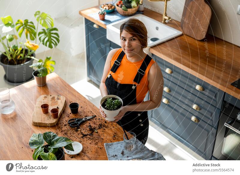 Zufriedene Gärtnerin mit Topfpflanzen in der Küche Frau Hausgarten vegetieren Pflanze kultivieren Tisch wachsen Gartenbau Blatt Wachstum organisch Flora Botanik